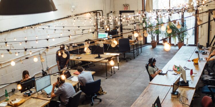 A busy coworking space where assistants are sitting at laptops and working together.